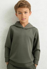 Oliwkowa bluza z kapturem, o wysokiej szyi i długich rękawach, wykonana z miękkiego materiału. Charakteryzuje się luźnym krojem i prążkowanymi mankietami.