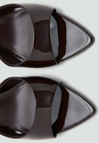 Zuecos de cuero de charol marrón oscuro con punta afilada y banda superior ancha. Textura suave y acabado brillante. Diseño minimalista sin hardware visible.