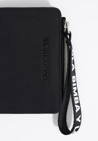 Zwarte stoffen portemonnee met reliëf "BIMBA Y LOLA" logo, ritssluiting en afneembare polsband met witte tekst. Gladde textuur.