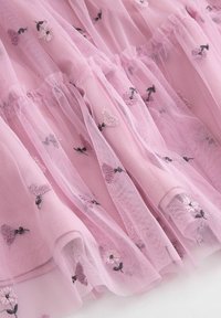 Różowy tiul z kwiatową haftacją. Materiał jest przejrzysty i teksturowany, z falbanami i rozmieszczonymi motywami kwiatowymi w ciemniejszych kolorach.