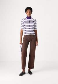 Top a maniche corte a righe viola e bianche con colletto alto; abbinato a jeans a gamba larga marroni. La modella tiene una pochette bianca e indossa mocassini neri.