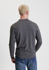 Grau langärmliges Hemd mit Kragen, aus weichem Material, mit gerippten Bündchen und Saum. Getragen mit blauen Jeans.