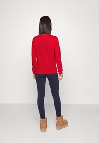 Sudadera roja, de textura suave, con puños ajustados, combinada con leggings azul marino y botas de tobillo color marrón claro, con punta redondeada y caña corta.
