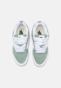 Grønne semskede sneakers med hvite snøringer og tunge. Har en kontrastfarget hvit side-stripe og polstret innside. Flat gummisåle som er synlig.