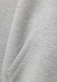 Ljusgrå sweatshirttyg med en borstad textur, med en sned söm och ett lagfickor på framsidan.