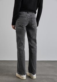 Jean en denim gris avec une coupe droite, léger délavage, et deux poches arrière. Porté avec des baskets blanches.