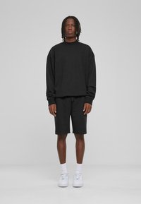 Sweat à capuche noir avec une coupe décontractée et un short, tous deux en matériau doux. Associé à des baskets blanches et des chaussettes à cheville.