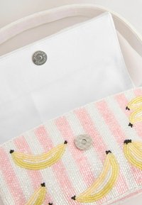 Sac à main blanc avec rabat perlé à rayures roses et blanches décoré de bananes perlées jaunes et fermeture à bouton magnétique.