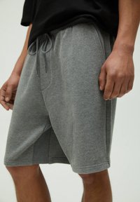 Shorts en mélange de coton gris avec une taille élastique et un cordon de serrage, poches latérales et coupe décontractée. Texture lisse avec des coutures discrètes.