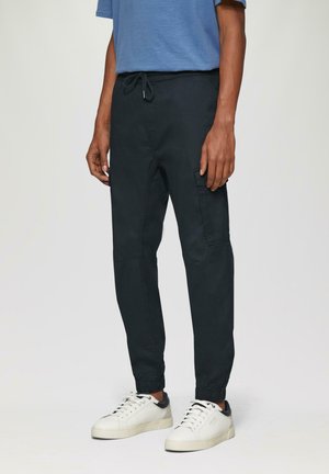 Zwarte taper joggers van ademend materiaal, met een elastische tailleband, koord en zijzakken. Gestyled met witte sneakers.