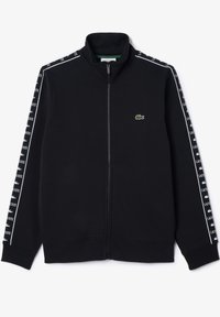 Veste noire zippée avec col haut, texte blanc "Lacoste" et logos crocodile sur les manches, petit logo crocodile vert sur la poitrine.