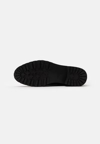 Black rubber sole with textured tread pattern featuring multiple grip sections and a subtle logo detail. Flat, durable design for traction.