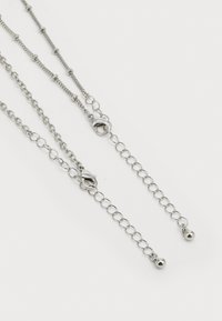 Chaîne en argent avec trois brins, présentant différents styles de maillons, des perles rondes et deux fermoirs près des extrémités pour une longueur ajustable.