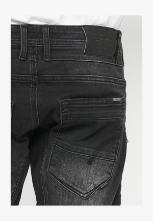 Fekete farmernadrág magas derékkal, jellegzetes varrásokkal és két hátsó zsebbel. A hátsó címke a márka részleteivel van domborítva.