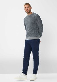 Grå strikketrøje med ribbet tekstur, parret med marineblå chinos og hvide sneakers. Outfitet har et afslappet design med en tætsiddende silhuet.