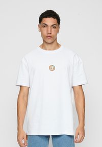 Hvid bomulds T-shirt med rund halsudskæring og korte ærmer, prydet med et farverigt logo centreret på brystet. Løs pasform.