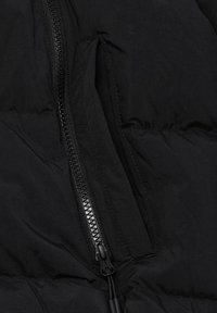 Zwarte pufferjacksectie met een stevige zwarte rits, een gladde nylontextuur en meerdere stikdetails langs de naden.