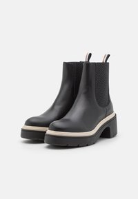Botas de tobillo de cuero negro con paneles laterales elásticos texturizados, tacón grueso y suela en contraste beige. Detalle de bucle en la parte trasera para facilitara la puesta.