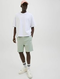 Witte oversized t-shirt, mintgroene shorts met logo aan de voorkant, witte sneakers met gestructureerde zolen en een roze pet. Zwart-wit gestreepte sokken.
