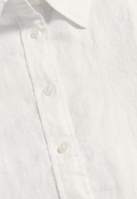 Weißes Leinenhemd mit Button-down-Kragen, fünf weißen Knöpfen und dezent gesticktem Logo auf der Brust. Glatte, leichte Textur.