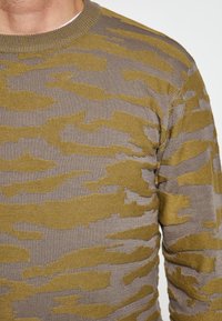 Pulover tricotat cu decolteu rotund, având un model de camuflaj în nuanțe de verde măsliniu și bej. Material texturat, de greutate medie.