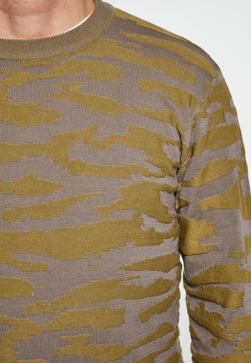 Pulover tricotat cu decolteu rotund, având un model de camuflaj în nuanțe de verde măsliniu și bej. Material texturat, de greutate medie.