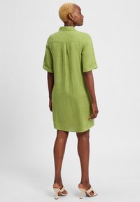 Grünes Leinenhemdkleid mit hochgekrempelten Kurzarm, Knopfkragen, Rückenpasse und lockerem Schnitt, das oberhalb des Knies endet.