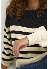 Randig tröja i svart och kräm, med ribbad struktur och breda ärmar. Framträdande med ribbad halsringning och manschetter.