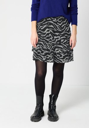 Jupe à motifs zébrés noir et gris avec un ourlet volanté, fabriquée en tissu léger, assortie à des bottines noires et des bas foncés.