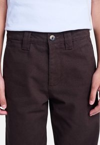 Pantalones marrones de mezcla de algodón con una textura suave, que cuentan con una cremallera frontal, cierre de botón, dos bolsillos laterales y pasadores para cinturón.