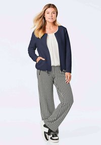 Marineblaue gesteppte Jacke mit rundem Ausschnitt und Taschen, kombiniert mit schwarzen und weißen Hahnentrittpants und schwarzen Sneakers.