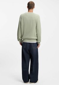 Suéter de punto verde claro con textura acanalada y hombros caídos, combinado con jeans azul oscuro de corte amplio y camisa blanca debajo.