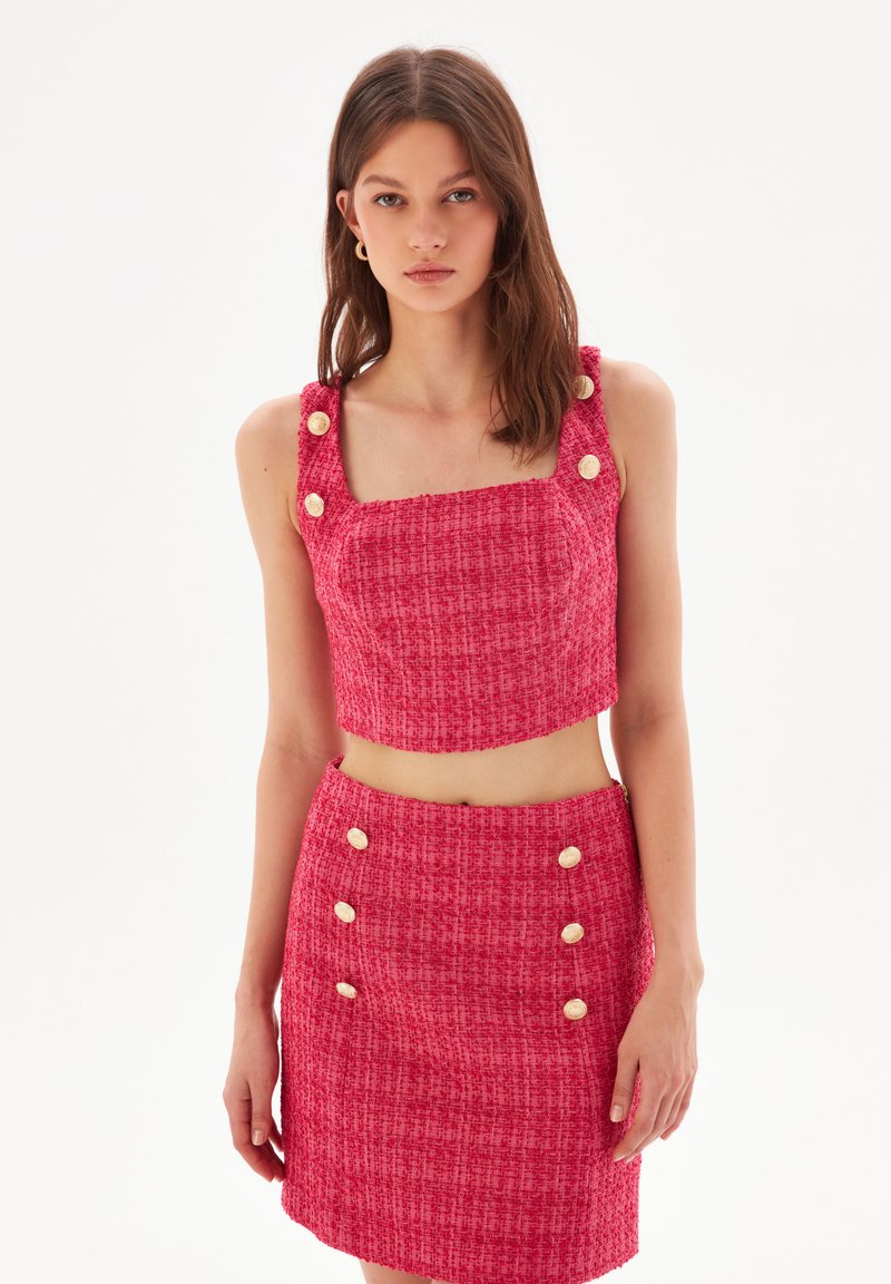 Top corto in tweed rosso con scollatura quadrata e grandi dettagli con bottoni. Abbinato a una gonna aderente coordinata con dettagli in bottone sul davanti.