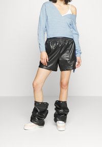 Suéter azul claro con diseño de hombro caído, combinado con pantalones cortos de cuero sintético negros con botones a presión y botas negras holgadas.