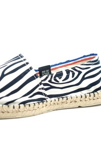 Espadrille en tissu rayé noir et blanc avec une semelle en jute. Dotée d'une étiquette sur le côté avec "ART OF SOULE". Doublure rouge et bleue visible.