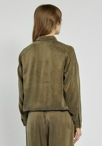 Oliwkowa, długosleeve koszula o luźnym kroju, miękkiej teksturze i zapięciu na guziki. Posiada prosty dół oraz detal w formie yoke z tyłu.