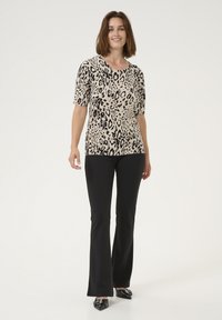 Leopard print top in beige and black, short sleeves, paired with black flared pants and pointed black shoes. Smooth, stretchy fabric.