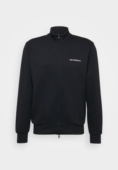 Black zip-up sweatshirt made of soft fabric. Features a high collar and ribbed cuffs, with a white logo on the left chest.