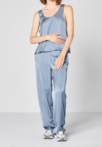 Světlomodrý saténový top bez rukávů a odpovídající kalhoty s volným střihem, které mají hladkou texturu. Nosí se s šedými teniskami.