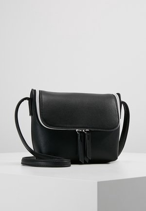 Sac bandoulière en cuir noir avec rabat zippé et double curseur, présenté sur un piédestal blanc sur fond gris.