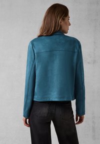 Teal faux suedejacka med en slät textur, rak skärning och krage. Har en söm över den övre ryggen och långa ärmar.