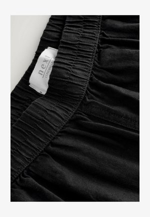 Black fabric with a gathered waistband, featuring a white tag labeled "next" and text indicating material composition. Smooth texture.