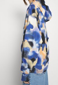 Felpa con cappuccio in blu, nero e arancione con motivi astratti; realizzata in tessuto morbido con una vestibilità rilassata e polsini e orlo a coste.