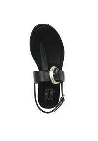 Sandale en cuir noir avec une semelle plate, dotée d'un entredoigt, d'une bride de cheville et d'une boucle circulaire en argent. Texture lisse, design minimal.