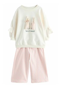 Weißes Sweatshirt mit zwei plüschigen Hasenapplikationen und dem Text "Lust auf eine Karotte?" kombiniert mit rosa-weißen gestreiften, weit geschnittenen Hosen.