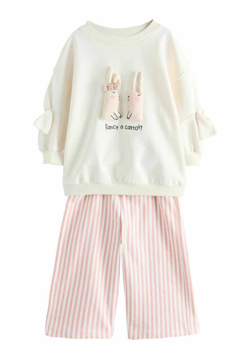 Weißes Sweatshirt mit zwei plüschigen Hasenapplikationen und dem Text "Lust auf eine Karotte?" kombiniert mit rosa-weißen gestreiften, weit geschnittenen Hosen.