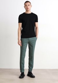 Zwarte t-shirt met korte mouwen gecombineerd met lichtgroene op maat gemaakte broek en zwarte veterschoenen. Minimalistisch ontwerp met een getailleerde pasvorm.