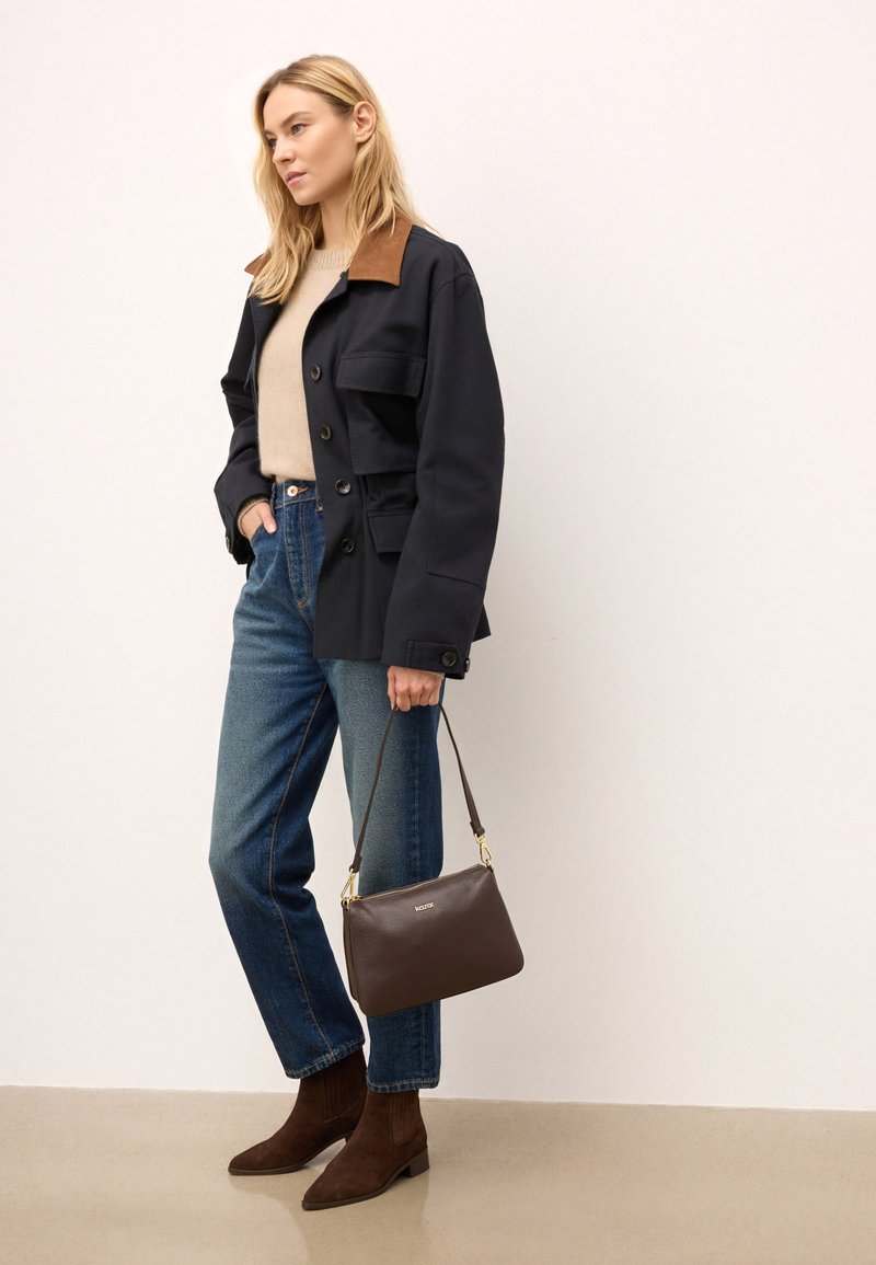 Granatowa kurtka z brązowym kołnierzem, beżowy sweter, niebieskie dżinsy z wysokim stanem, brązowa skórzana torebka i brązowe zamszowe botki za kostkę. Gładkie faktury.