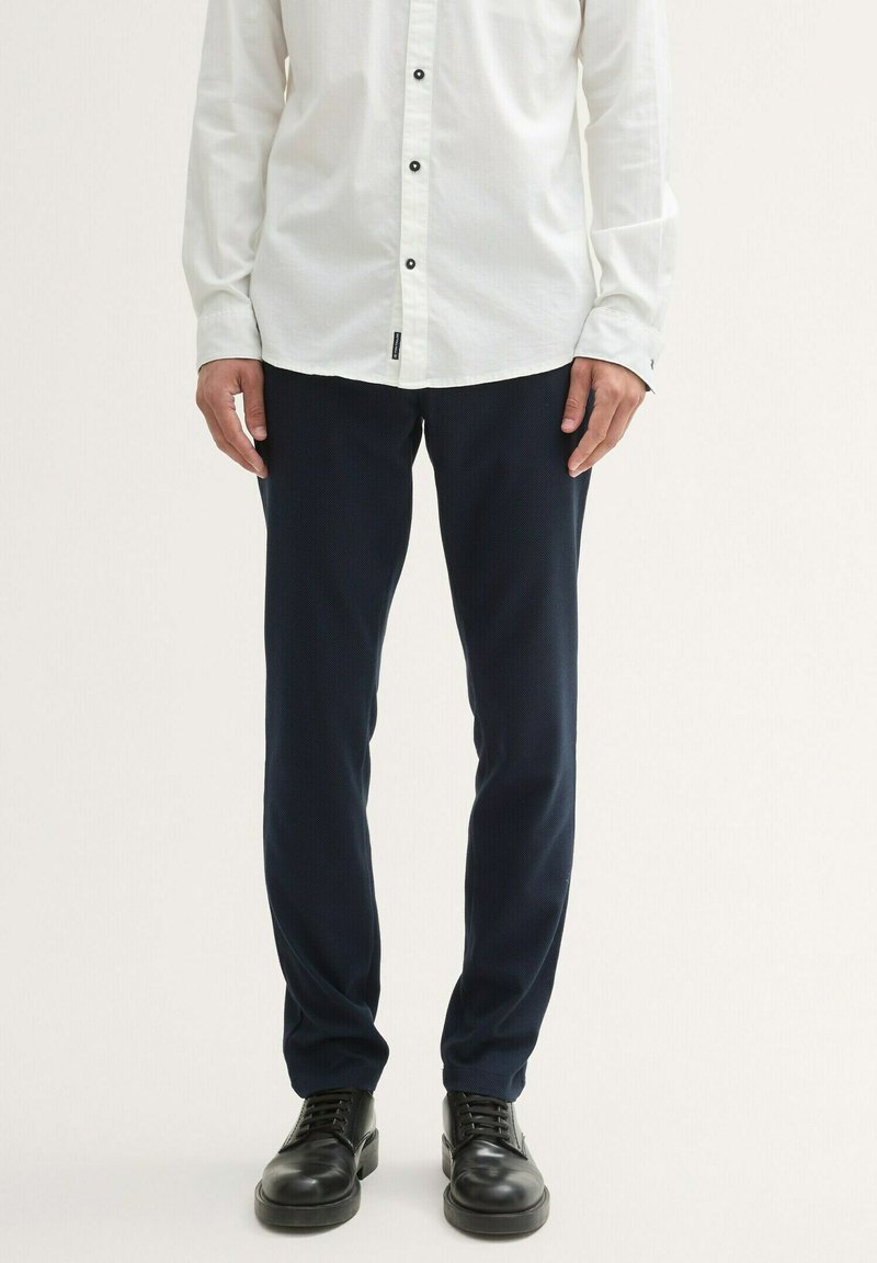 Navy blue trousers with a textured fabric, paired with a white long-sleeve button-up shirt featuring black buttons and a structured fit.