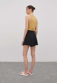 Een tan kleurige mouwloze top, zwarte flared rok en witte slidesandalen. Gladde textuur, getailleerde top en een relaxte fit in de rok.